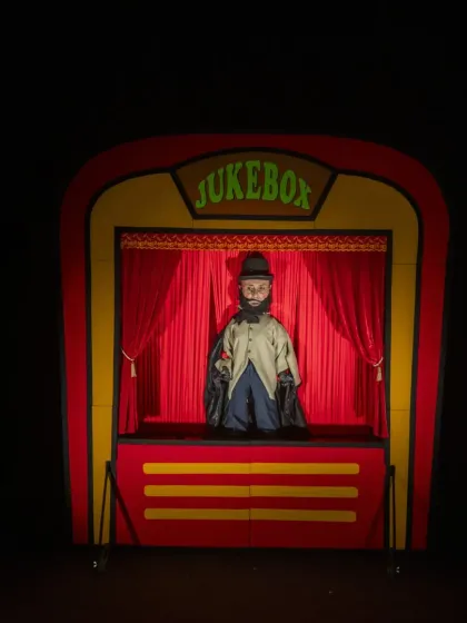 A dapper, top-hatted character appears in the 'Jukebox' puppet theatre, ready to perform a song for the delighted audience.