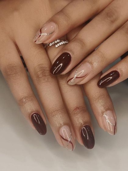 An elegant design pairing solid maroon nails with nude accent nails featuring a delicate, glittery swirl. This is a perfect look for autumn or a special evening out.