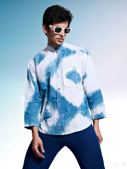 A studio shot for a menswear brand specializing in hand-printed garments. The model wears a tie-dye indigo shirt, and the clean, gradient background makes the unique pattern and colors pop.