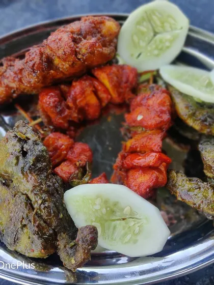 A close-up of our mixed non-veg starter platter. It includes spicy red chicken tikka, green hariyali fish, and seekh kebabs, served with fresh cucumber slices for a complete appetizer experience.
