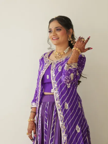 A full view of the bride's vibrant purple outfit. The makeup is kept bright and fresh, with a focus on her happy, smiling expression.