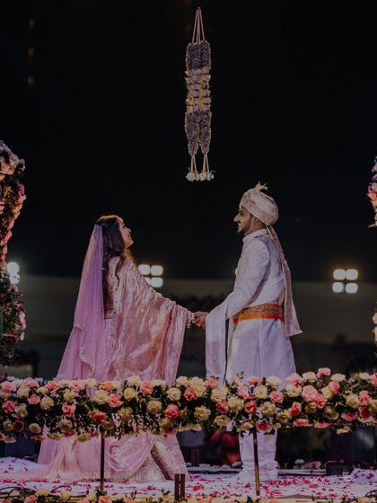 The couple holding hands on the flower-adorned stage, a moment of connection before the festivities begin.