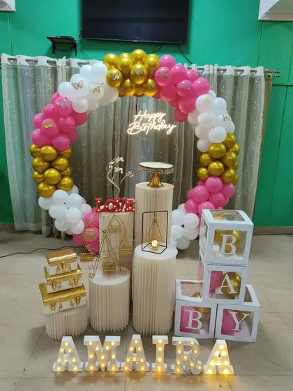 This pink, white, and gold balloon ring decor creates a warm and inviting atmosphere for a birthday celebration, personalized with the name 'Amaira' in lights.