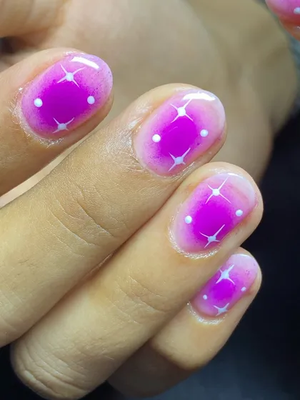 A fun and sparkly aura nail design in bright magenta with little white starbursts.