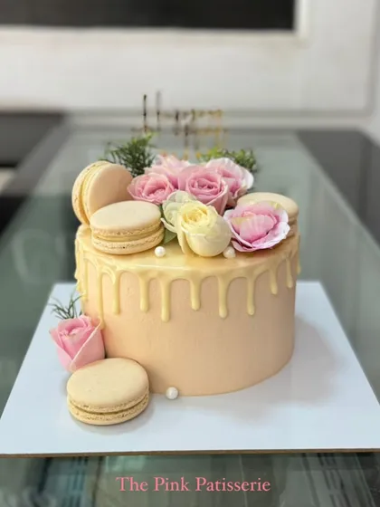 A peach-colored drip cake adorned with fresh flowers and macarons.
