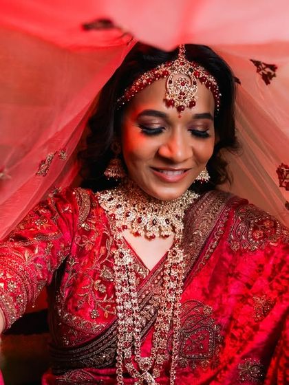 A bride lifts her red veil, revealing a beautiful smile.