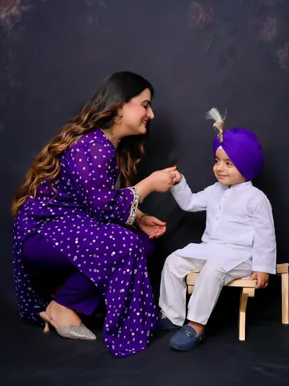 A mother shares a sweet, interactive moment with her son, who is dressed in a traditional kurta and turban. This photo highlights the beautiful bond between mother and child.