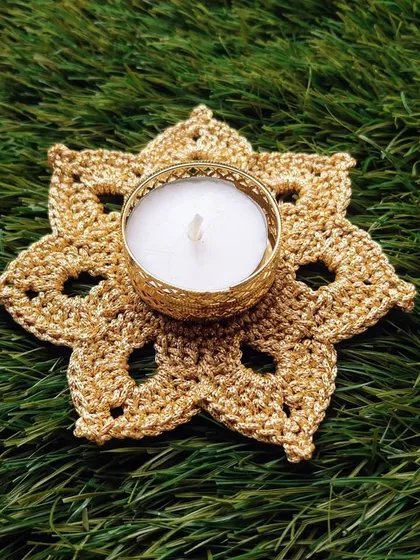 A single golden tea light holder with a white candle, placed on a natural green background. The simple elegance of this piece shines through.