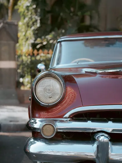 A close-up of the front headlight and chrome bumper of a vintage car. I focus on these details to appreciate the artistry and design of classic automobiles.