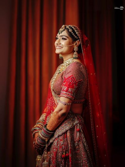 An elegant three-quarter portrait of the bride. Her classic red lehenga and confident smile make for a stunning and timeless image.