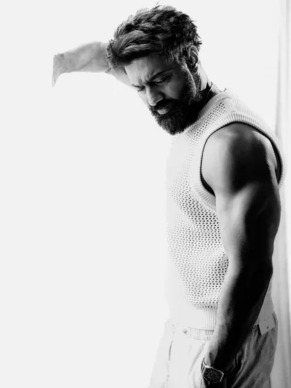 An introspective black and white shot of Dev. His downward gaze and the dramatic shadows create a quiet, emotional moment, showcasing a more vulnerable side.