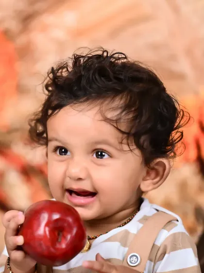 A close-up of a happy baby boy holding an apple during an outdoor shoot.