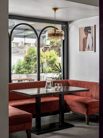 To create intimate dining experiences, I designed this private nook. I replaced a solid wall with a metal-framed archway, bringing in light and connecting it to the outdoors. The cozy rust-brick colored sofa adds warmth and comfort.