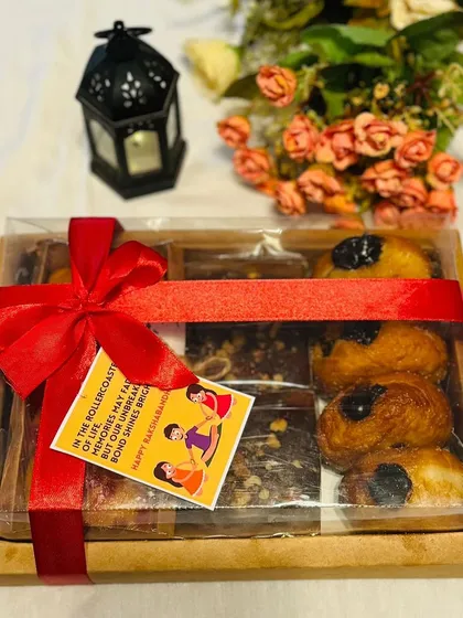 A beautifully presented gift box tied with a red ribbon, perfect for Rakhi. This clear-lid box shows a mix of brownies and doughnuts, complete with a festive tag.