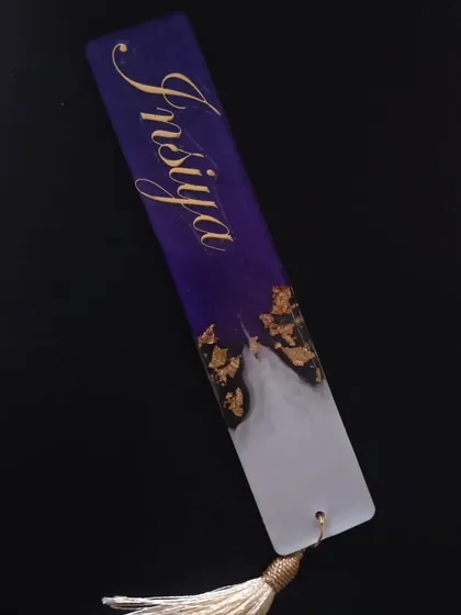 A beautiful deep purple and white bookmark for 'Insiya', with delicate gold leaf accents and a white tassel.