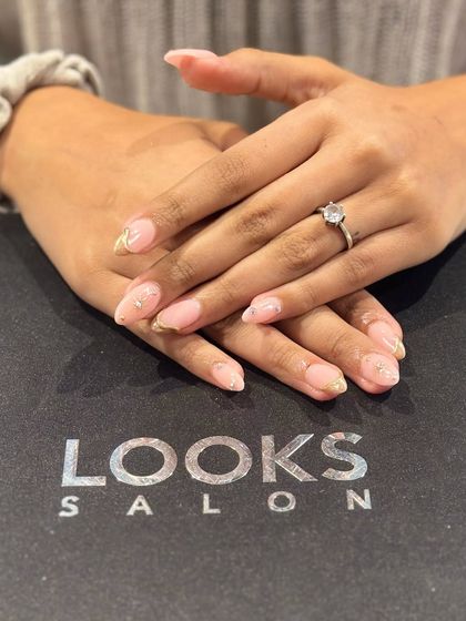 A soft and romantic nail design. This look features a sheer pink base with delicate gold leaf accents on the tips, creating a subtle yet luxurious effect.