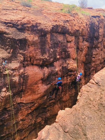 Multiple climbers practice their skills on a vast cliff face, showcasing the scale of our outdoor classroom in Badami.