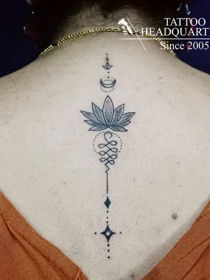 A beautiful Unalome tattoo on the spine, symbolizing the path to enlightenment. The design incorporates a lotus flower, representing purity and spiritual awakening.