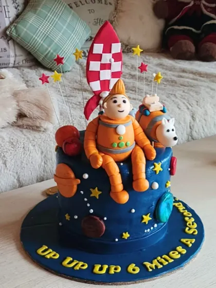 An out-of-this-world space adventure cake with a fondant astronaut and his dog, a rocket ship, and a galaxy of stars and planets.