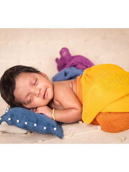A colorful and happy portrait of a sleeping baby. Wrapped in bright, multi-colored fabrics, the newborn dreams away on a soft, textured blanket, radiating pure joy.