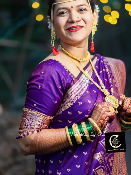 A full view of the bride's look, showcasing the elegant purple saree, traditional gold jewelry, and the complete makeup and hair styling I provided. You can also see the beautiful dark stain from her bridal mehendi.