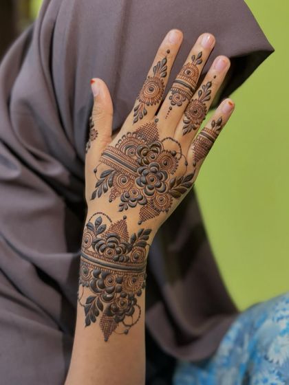 A beautiful party henna design on the back of the hand, with a floral cuff and delicate finger details.