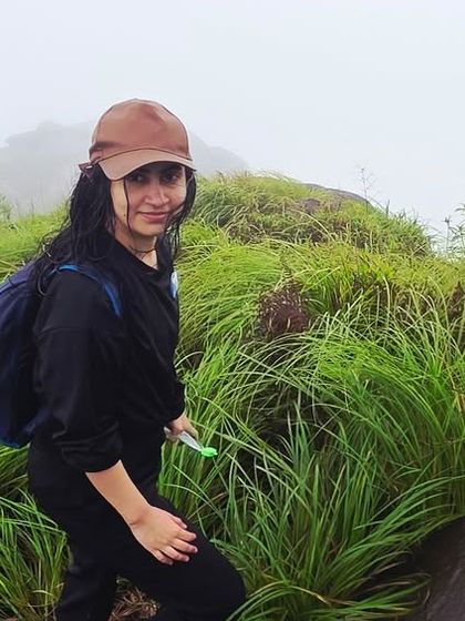 A trekker making her way through the tall, vibrant green grass on the slopes of Kurinjal, with the mist-covered peak in the background.