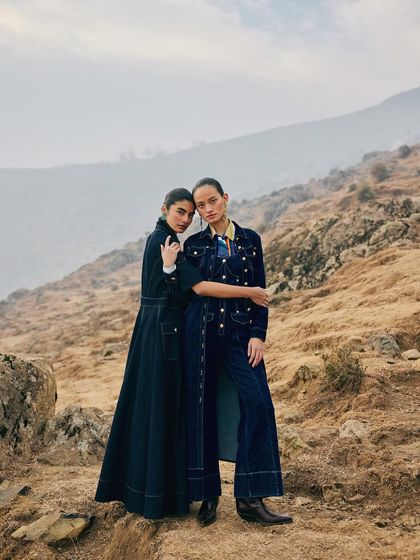 Two models styled in complementary denim looks for Ani Clothing. Their pose suggests a story of sisterhood and shared journeys against a vast, hilly landscape.