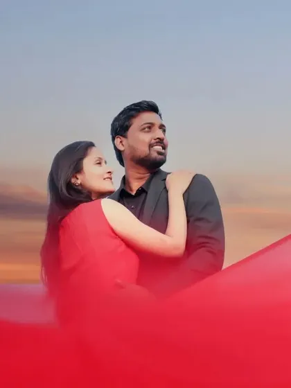 A dramatic pre-wedding shot where a flowing red fabric elegantly frames the couple against a beautiful sunset sky, creating a cinematic and artistic portrait.