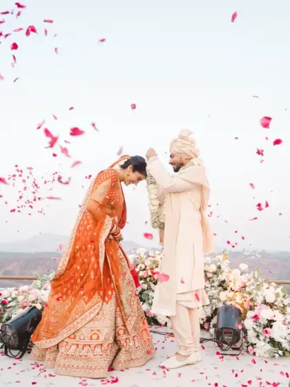 A shower of rose petals rains down on the couple during their varmala exchange. This beautiful, candid moment is full of color, emotion, and celebration.