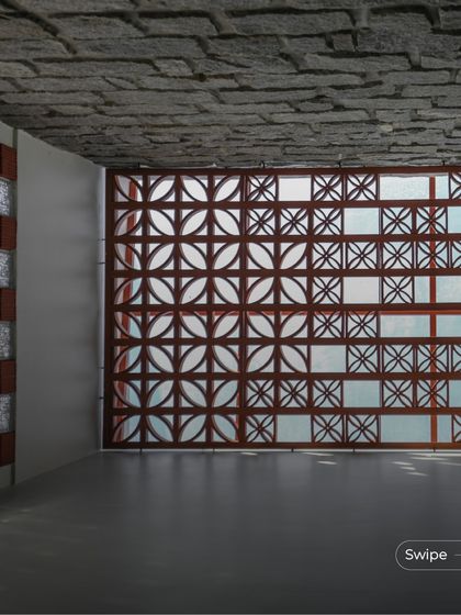 The play of sunlight through a terracotta jali screen at the Shashidhar Residence. The combination of the patterned screen, glass blocks, and stone-finished ceiling creates a rich and textured interior space.