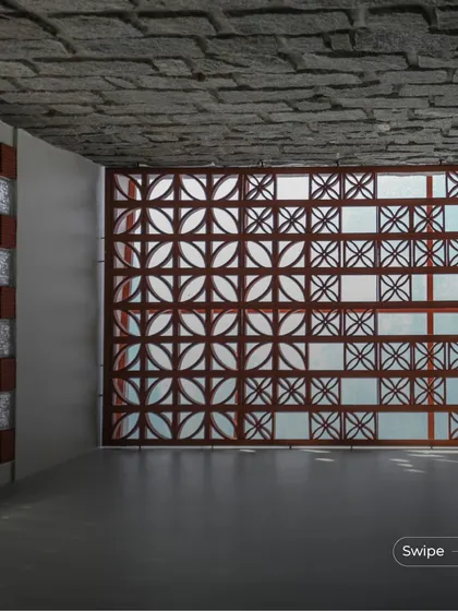 The play of sunlight through a terracotta jali screen at the Shashidhar Residence. The combination of the patterned screen, glass blocks, and stone-finished ceiling creates a rich and textured interior space.