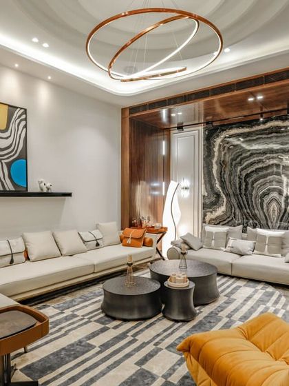 This contemporary living room at our Vikaspuri project features a bold, book-matched marble wall that acts as a piece of natural art. The space is furnished with a large sectional sofa, a unique orange lounge chair, and a geometric-patterned rug.