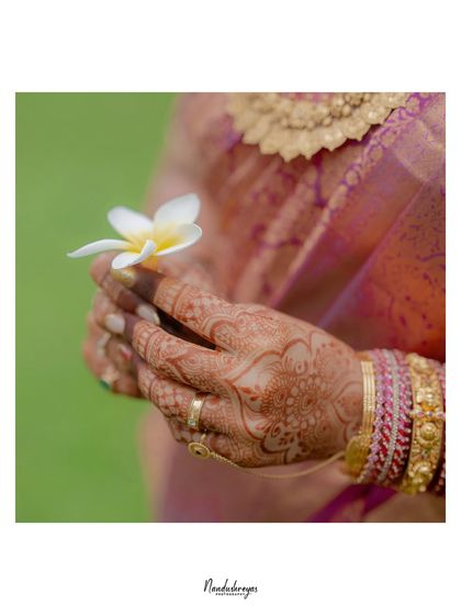 A delicate close-up of the bride's hands, adorned with intricate henna and holding a single white flower. A symbol of purity and new beginnings.
