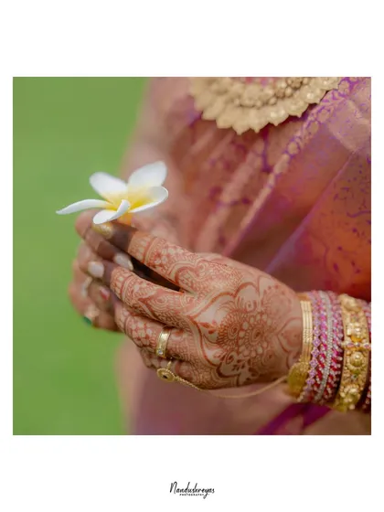 A delicate close-up of the bride's hands, adorned with intricate henna and holding a single white flower. A symbol of purity and new beginnings.