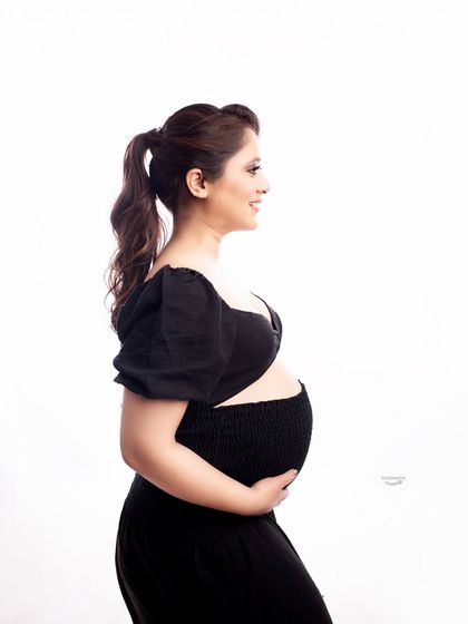 A simple and modern profile shot. The client is wearing a stylish black two-piece outfit against a clean white background, highlighting her baby bump in a contemporary way.