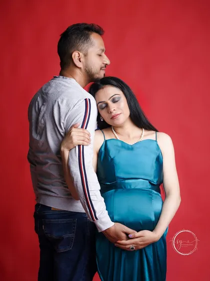 A quiet, intimate pose against a bold red backdrop. This maternity photo highlights the peaceful connection between the couple, with the mother-to-be resting gently on her partner's shoulder.