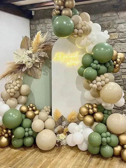 An elegant and earthy baby shower design. This setup uses a sophisticated palette of olive green, beige, and gold balloons, complemented by dried pampas grass and a custom neon sign for a modern, natural vibe.