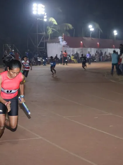 A relay runner powers through her leg of the race under the floodlights, showcasing speed and teamwork.
