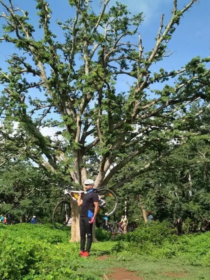 Sometimes you just have to carry your bike to get that perfect victory shot. A rider posing with his cycle amidst the lush greenery of a forest trail.