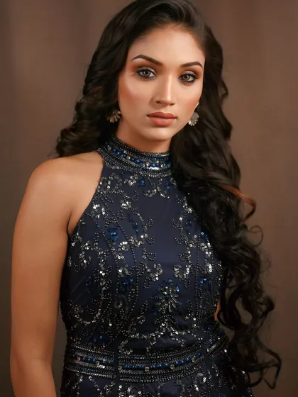 A stunning reception or cocktail party look in a deep blue gown. The makeup is focused on a sharp, winged eyeliner and glowing skin to match the sophisticated outfit.
