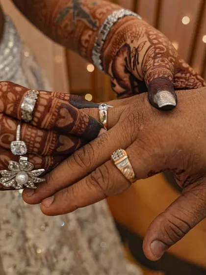 This photo captures the moment of the ring exchange. The bride's intricately designed mehendi is beautifully displayed as she places the ring on her partner's finger.