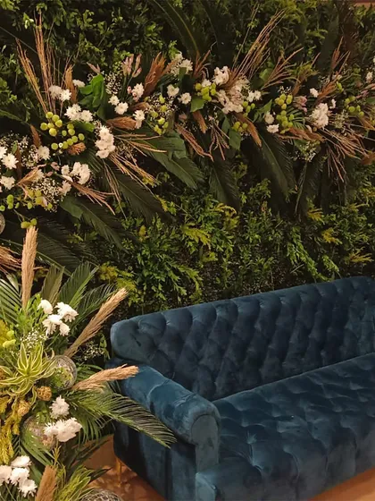 A close-up of a lounge corner with a luxurious blue velvet sofa set against a green foliage wall. This type of stylish seating area provides a comfortable and photogenic spot for guests to relax.