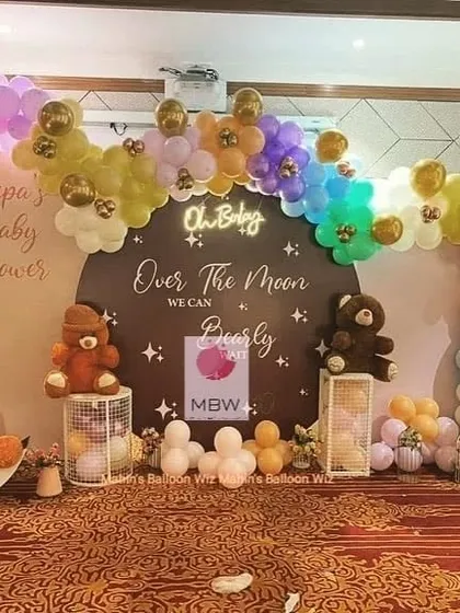 An "Over the Moon We Can Bearly Wait" baby shower. This cozy setup features teddy bears on pedestals and a rainbow-colored balloon arch with gold accents.