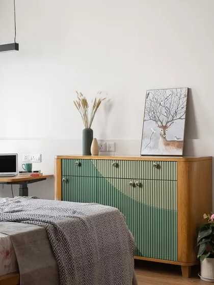 Opposite the bed, a custom-made fluted chest of drawers in shades of green serves as a statement piece. Next to it, a compact study nook provides a functional workspace.