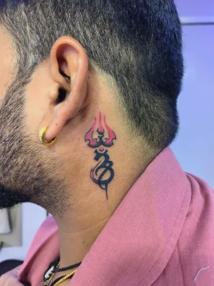 A Trishul and Om symbol tattoo placed behind the ear. This is a popular spot for smaller spiritual tattoos that are both discreet and powerful.