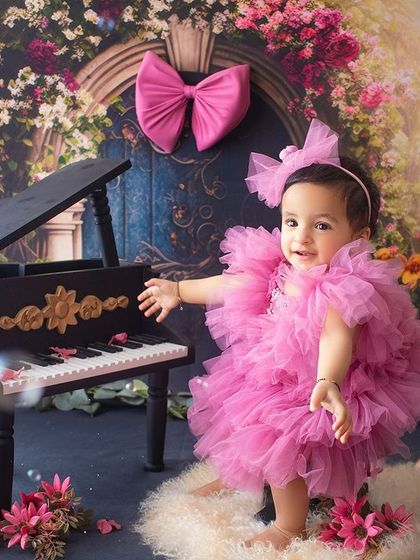 A magical first birthday scene with a miniature piano, a floral archway, and floating bubbles. This little girl in her bright pink dress looks like she's in a fairytale.