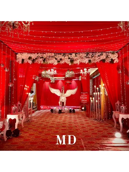 Another view of the dramatic red-themed entrance. The pathway is lined with elegant tables and lanterns, leading guests towards the main event under a canopy of red drapes and fairy lights.