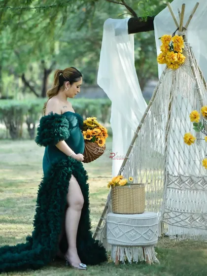 A side profile of the mom-to-be in a green ruffled gown, holding a basket of sunflowers. This image highlights the props and styling I provide for themed outdoor photoshoots.