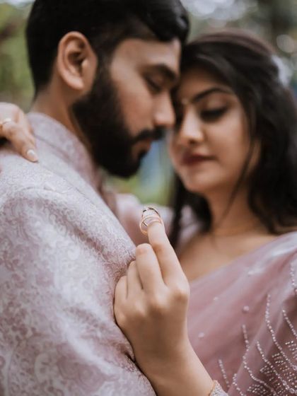 A beautifully composed close-up focusing on the engagement ring. The soft focus on the couple in the background keeps the emotion central to the image.
